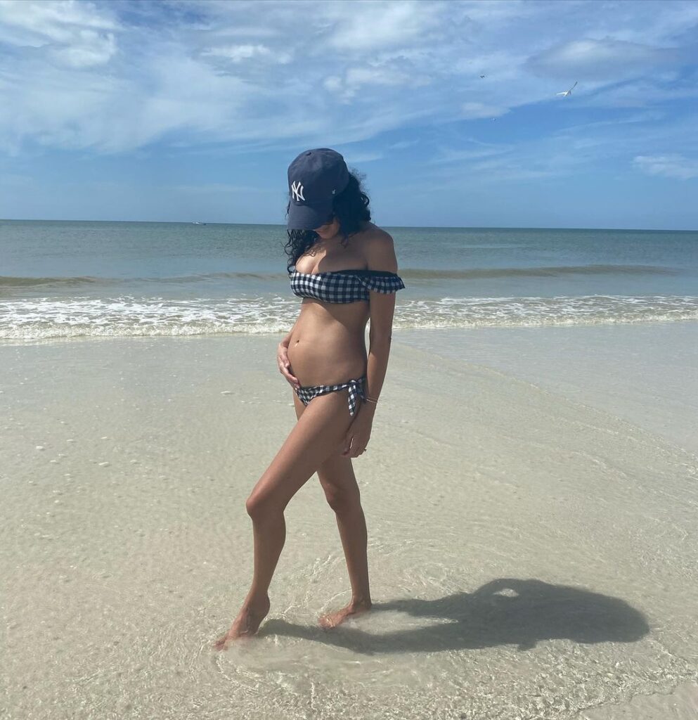 Actress wearing a black-and-white gingham bikini and a Yankees cap while hugging her growing belly | Pic source: